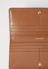 Unutrašnjost smešnog novčanika od smešnog kožnog materijala s višestrukim utorima za kartice. Zlato akcenti s utisnutim logotipom "MICHAEL KORS". Glatka tekstura, minimalistički dizajn.