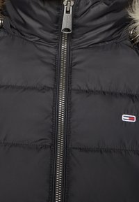 Chaqueta acolchada negra con un alto cuello, con un cierre de cremallera plateado. Incluye un logo en rojo, blanco y azul en el lado izquierdo.