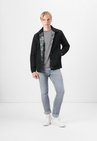 Veste noire avec une doublure intérieure à motif, t-shirt gris, jean bleu clair et baskets blanches. La veste a un col et une fermeture à bouton.