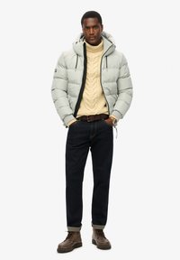 En pufferjakke i lys grå med en sort lynlås, båret over en cremet kabelstrikket sweater, parret med mørke jeans og brune snørebåndsstøvler.