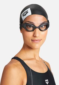 Gorro de natación de silicona negra y gafas de natación negras con un acento rosa. El nadador lleva un traje de baño de una sola pieza negro con detalles de costura blanca.