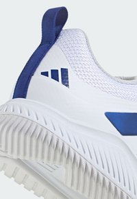 Biały but sportowy z teksturowaną siateczkową cholewką, niebieskimi akcentami oraz wzorzystą gumową podeszwą z głębokimi rowkami zapewniającymi przyczepność.