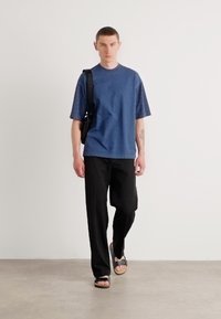 Camisa azul de manga corta con mangas de panel texturado, pantalones anchos negros y sandalias negras. Diseño minimalista con un ajuste moderno.
