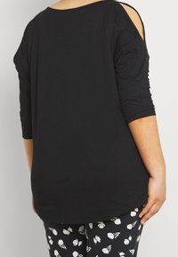 Sort oversized top med mellemlange ærmer og udskårne skulderdetaljer, lavet af blødt stof, parret med mønstrede blomster leggings.