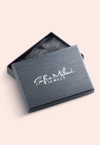 Grå texturerad smyckeskrin med öppen lock, med "Sofia Milani" i vit skrivstil och en svart inredning med skrynkligt silkespapper.