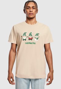 Beige bomulds t-shirt med et "Juletre" grafik. Tre nisser i grønne og ternede hatte, med accenter af rød og hvid.