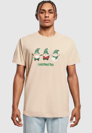 Beige kokvilnas t-krekls ar "Ziemassvētku trio" grafiku. Trīs gnomi zaļās un gaiši zaļās cepurēs, ar sarkaniem un baltiem akcentiem.