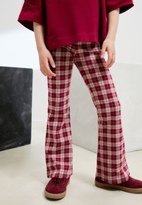 Rote karierten Schlaghosen aus weichem Stoff, mit einem Muster aus tiefroten und beigen Quadraten, kombiniert mit passenden burgunderfarbenen Schuhen.