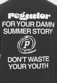Černé bavlněné tričko s výrazným bílým textem: "Pegador," "PRO TVŮJ ZATRACENÝ LETNÍ PŘÍBĚH," a "NEPLÝTVEJ SVOU MLADOSTÍ," s kulatým logem.