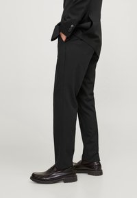 Svarta skräddarsydda byxor med en slät yta, slim fit och en veck framtill. Bärs tillsammans med blanka svarta loafers med en tjock sula.