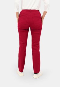 Rote, eng anliegende Hose aus glattem Material, mit zwei Gesäßtaschen und einem dehnbaren Bund. Kombiniert mit weißen Sneakers.