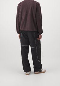 Maglione in pile oversize di colore viola scuro con spalle scese, abbinato a pantaloni neri con cuciture bianche a contrasto e una vestibilità comoda.