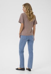 Kortærmet brun top lavet af blødt stof, parret med lyseblå lige ben jeans og sorte flade sko. Enkel design uden synlige mønstre.
