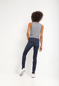 Blå denim skinny jeans med bakfickor och subtila sömnadsdetaljer, kombineras med en grå randig linne, sedd bakifrån.