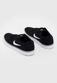 Pár černých nízkých tenisek Nike s bílými podrážkami a bílými logy swoosh, zobrazených z pohledu zezadu v úhlu tří čtvrtin na bílém pozadí.