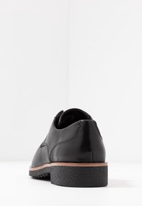 Chaussures en cuir noir avec une finition lisse, présentant un bout arrondi, un talon bas et une semelle en caoutchouc texturée. Des coutures discrètes soulignent le design.