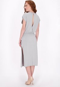 Grijze, middellange jurk met kapmouwen, een keyhole aan de achterkant en zijsplitten. Elastische taille en zachte textuur, gecombineerd met nude hoge hakken.