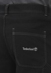 Shorts cargo en tissu noir avec coutures blanches contrastantes, arborant un logo Timberland brodé sur la poche arrière.