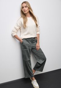 Light cream cable-knit sweater with ribbed cuffs paired with dark gray wide-leg trousers featuring front pockets and a soft texture.