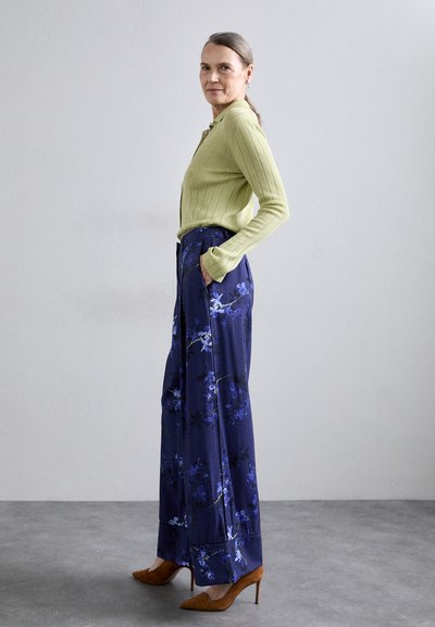 Light green ribbed cardigan with a button front paired with wide-legged navy pants featuring a floral print. Brown pointed heel shoes.