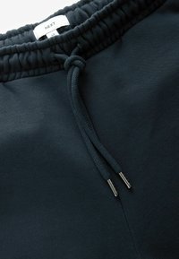 Joggers de un oscuro color azul marino con una cinturilla elástica, cordón ajustable y puntas de metal. Fabricados con un tejido suave y liso. La etiqueta dice "NEXT M."