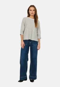 Stribet grå og hvid bomulds top med lange ærmer, parret med brede blå denim jeans. Sorte sko fremhæver outfittet.