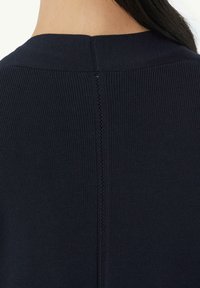 Marineblaues geripptes Strickoberteil mit einem Schiffsausschnitt, Rückennaht mit kleinen Ösen und einer glatten Textur.