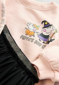 Lichtroze sweatshirt met een ribbelboord en een graphic van cartoonvarkens in kostuum. Zwarte rok met een geplooide textuur aan de onderkant.