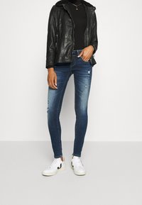 Chaqueta de cuero negra, top negro ajustado, jeans skinny azules con detalles desgastados y zapatillas blancas con acentos negros.