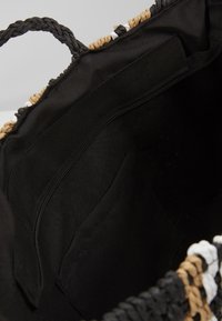 Wnętrze czarnej torby materiałowej z kieszonką na zamek i otwartą kieszonką, z plecionymi uchwytami w czarnym, brązowym i białym kolorze.