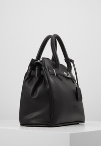 Schwarze Ledertasche mit doppelten Griffen, silberner Schnallenverzierung und angehängtem kleinem Beutel, auf einer weißen Oberfläche vor grauem Hintergrund platziert.
