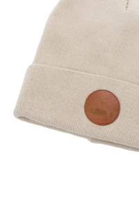 Beżowa czapka dziana z podwiniętym mankietem i okrągłą brązową skórzaną łatką z górskim wzorem oraz sylwetką niedźwiedzia.