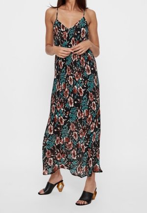 Vestido maxi negro con estampado floral, con tirantes finos y un vibrante patrón floral en rojo y azul verdoso. Combinado con tacones negros de punta abierta y detalles de madera.