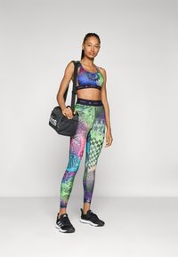 Färgglad sportbh och leggings med abstrakta mönster och rutigt mönster, i kombination med svarta träningsskor och en svart väska.
