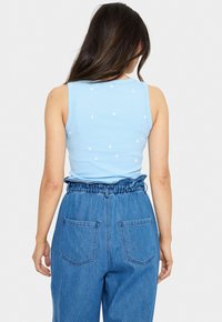 Ljusblå ribbad linne med vita hjärttryck, tillsammans med högmidjade blå denimbyxor med infällda detaljer i midjan och bakfickor.