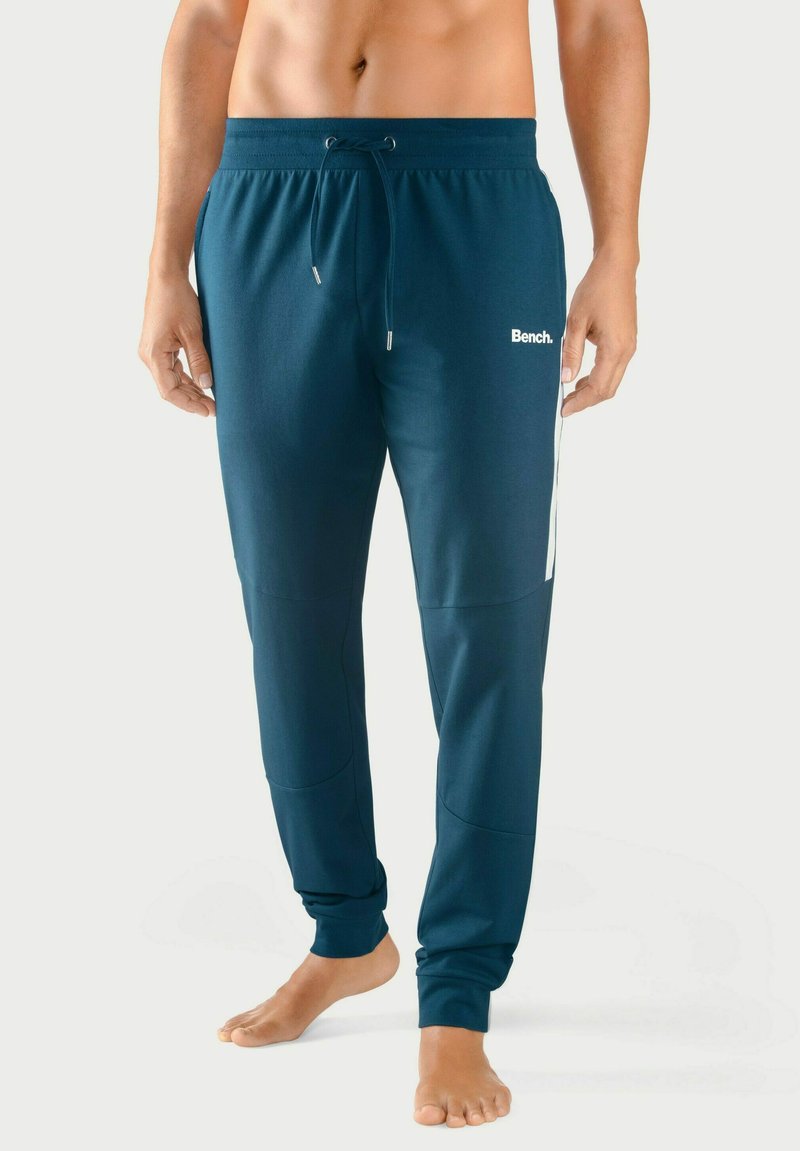 Teal Jogginghosen mit einem Kordelzugbund, schmal zulaufenden Bündchen und weißen seitlichen Streifen. Zeigt ein Logo auf dem linken Oberschenkel. Aus einem glatten Stoff gefertigt.