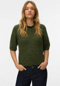 Krótki rękaw, zielony sweter dziany o fakturowanym wykończeniu. Posiada okrągły dekolt i prosty krój, zestawiony z ciemnymi dżinsami.