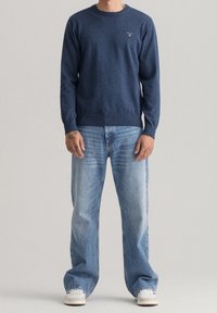 Marineblaues Sweatshirt mit langen Ärmeln und Rundhalsausschnitt, kombiniert mit hellblauen Jeans. Auffälliges Logo auf der Brust, Baumwolltextur.