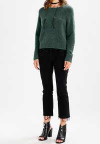 Groene fluffy trui, zwart cropped jeans met rafelige zoom, en zwarte open teen haklaarzen met rits aan de zijkant. Eenvoudige accessoires inbegrepen.