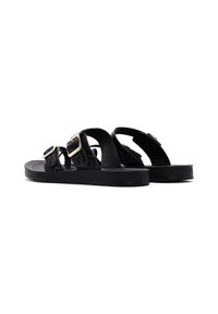 Sandales noires avec deux larges sangles texturées et des boucles contrastantes, ainsi qu'une semelle épaisse et plate. Le design est minimaliste et moderne.