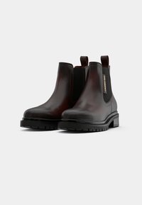 Botas Chelsea de couro castanho com painéis laterais elásticos e abas de puxar, apresentando uma sola preta espessa e um discreto detalhe de logotipo na lateral.