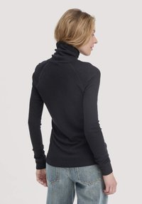 Schwarzer Rollkragenpullover mit langen Ärmeln, gerippter Textur, tailliertem Design und kontrastierenden Nahtdetails. Kombiniert mit hellblauen Jeans.