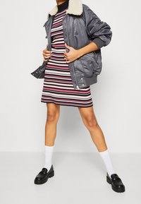 Giacca bomber grigia con colletto in pelliccia sintetica, abbinata a un vestito in maglia a righe con sfumature di rosa e nero. Scarpe platform nere completano il look.