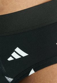 Mustat urheilushortsit sileällä pinnalla, joissa on leveä joustava vyötärö ja valkoiset logokorostukset sivuilla.