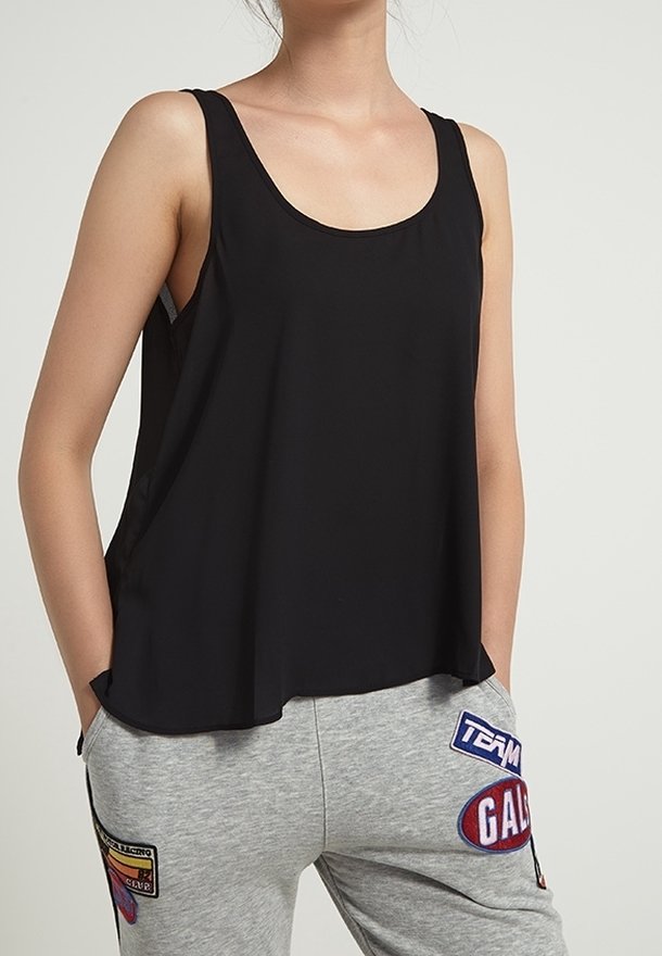 Top senza maniche nero con scollo rotondo, realizzato in tessuto morbido. Abbinato a pantaloni della tuta grigi con toppe colorate e loghi.