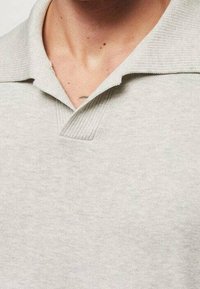 Polo shirt gris clair en tissu tricot doux. Doté d'un col classique, d'une patte de boutonnage en V et d'accents côtelés au niveau du col et de l'ourlet.