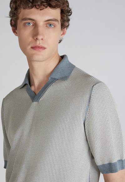 Sweter polo o fakturowanym splocie w jasnoszarym kolorze z niebieskim kołnierzykiem. Posiada krótkie rękawy i dekolt w kształcie litery V, wyeksponowany na charakterystyczny wzór.