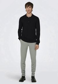 Camisa polo preta de manga longa com colarinho, combinada com calças justas cinzas claras e botas de tornozelo pretas. Textura de tecido suave, design minimalista.