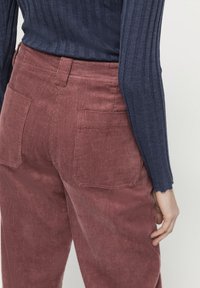 Kamelbruna kordbyxor med en subtil ribbad struktur. Har två bakfickor och är kombinerade med en navyblå långärmad tröja.