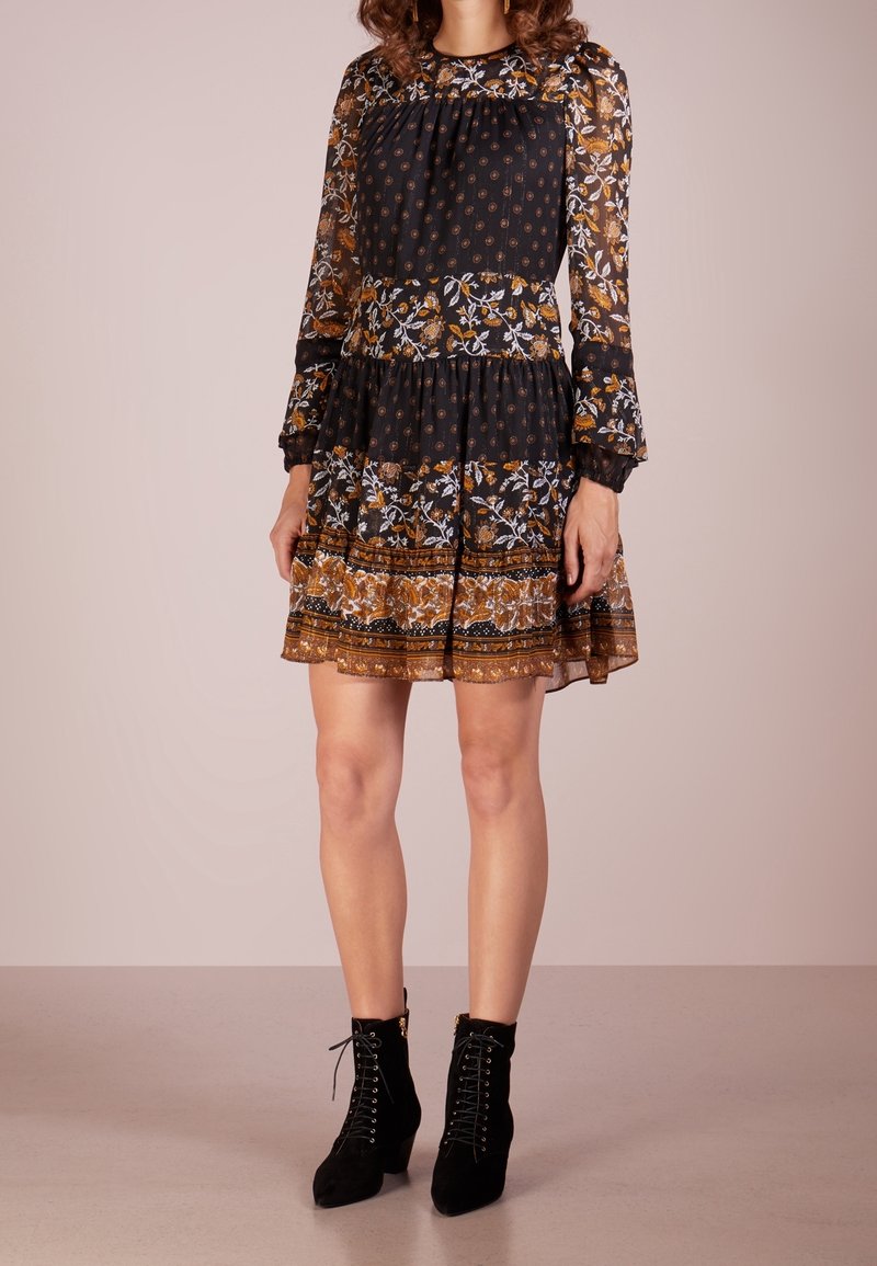 Femme portant une robe noire mi-longue aux motifs floraux et à pois, associée à des bottines noires à lacets.